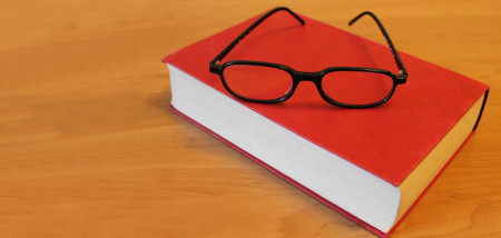 Ein orangefarbenes Buch mit einer schwarzen Brille liegt auf einem Tisch.