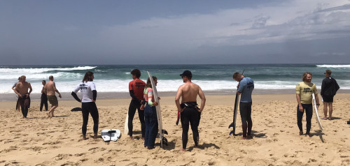 Gruppe an Menschen steht am Strand und bereitet sich auf das Surfen vor
